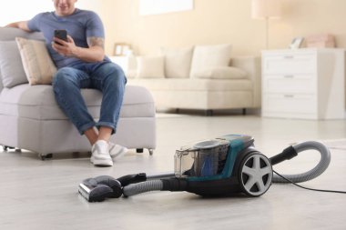 Evdeki koltukta akıllı telefonu olan adam, elektrik süpürgesine odaklan.