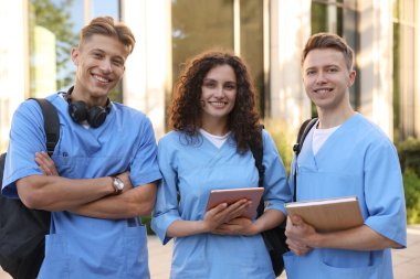 Açık hava binası yakınlarında üniformalı mutlu tıp öğrencileri.