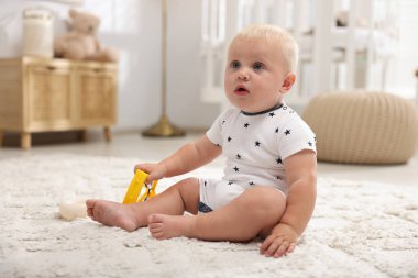 Işık odasında halıdaki oyuncakla oynayan sevimli bir bebek.