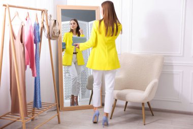 Hazırlanıyor. Evde aynanın yanında kıyafet deneyen genç bir kadın.