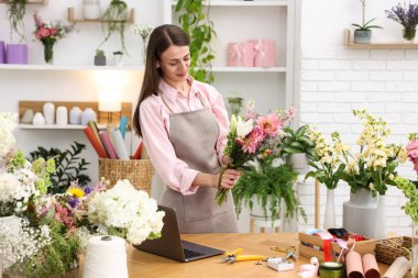 Profesyonel çiçekçi dükkandaki ahşap masada çiçek buketi yapıyor.