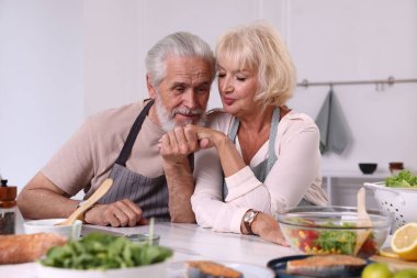 Evde yemek pişirirken el ele tutuşan yaşlı bir çift.