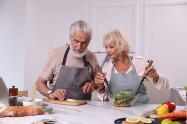 Yaşlı çift mutfaktaki mermer masada birlikte yemek pişiriyor.
