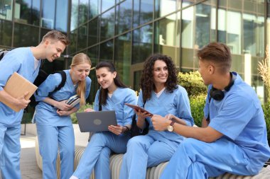 Üniformalı bir grup tıp öğrencisi açık hava binasının yakınında birlikte okuyorlar.