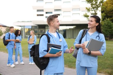 Sırt çantalı ve defterli tıp öğrencileri açık havada, seçici bir odak noktası.