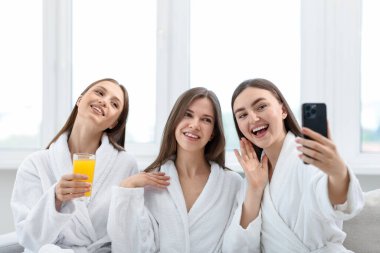 Bornozlu mutlu kadınlar spa salonunda selfie çekiyorlar.