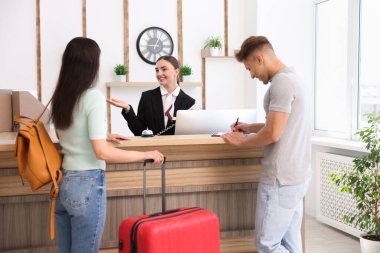 Otel resepsiyonunda müşterilerle çalışan gülümseyen bir resepsiyonist.