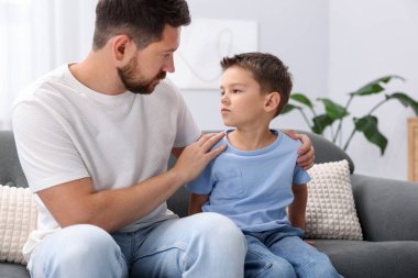 Baba evdeki kanepede üzgün oğlunu destekliyor.