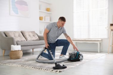Evdeki adam elektrik süpürgesini açıyor.