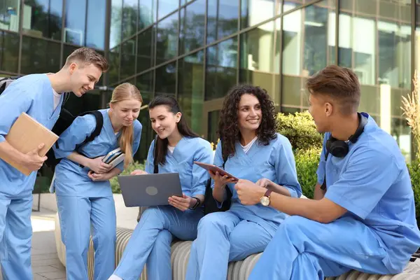 Üniformalı bir grup tıp öğrencisi açık hava binasının yakınında birlikte okuyorlar.