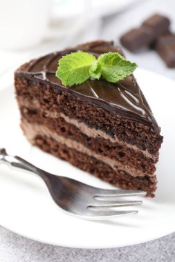 Bir parça lezzetli çikolatalı pasta, üzerinde nane ve çatal, yakın plan.