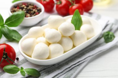 Lezzetli mozzarella peyniri, domates, fesleğen ve baharatlar beyaz ahşap masada, yakın plan.