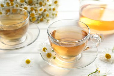 Cam fincanlarda romatik çay ve beyaz ahşap masada papatya çiçekleri, yakın plan.