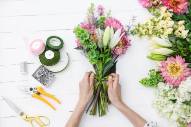 Çiçek buketi yapan bir çiçekçi, beyaz ahşap masa, üst manzara