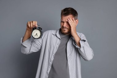Çalar saati olan bir adam gri arka planda akşamdan kalma.