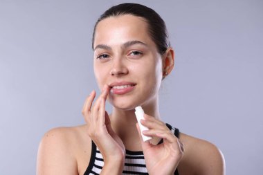 Açık gri arkaplanda dudak kremi olan genç bir kadın.