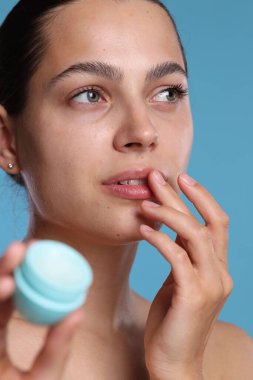 Açık mavi arka planda dudak merhemi olan genç bir kadın.