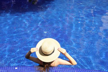 Güneşli bir günde, açık havada havuzda hasır şapkalı bir kız.