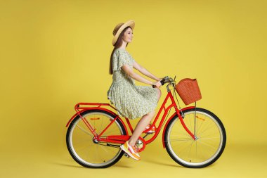 Açık yeşil arka planda sepeti olan şapkalı, gülen bir kadın.