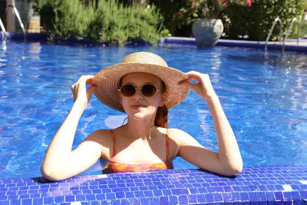 Güneşli bir günde yüzme havuzunda hasır şapkalı bir kız.
