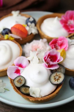 Lezzetli tatlı. Kremalı tartlar, böğürtlenler ve çiçekler ahşap masada, yakın plan.
