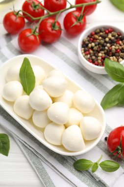 Lezzetli mozzarella peyniri, domates, fesleğen ve baharatlar beyaz ahşap masada, üst tarafta.