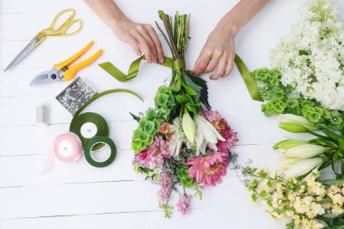 Çiçek buketi yapan bir çiçekçi, beyaz ahşap masa, üst manzara