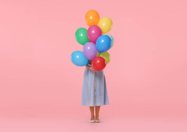 Pembe arka planda renkli balonların arkasına saklanan bir kadın.