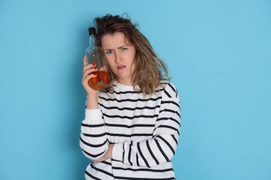 Bir şişe alkollü içki içen kadın açık mavi arka planda akşamdan kalma.