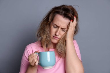 Gri arka planda akşamdan kalma kahve içen bir kadın.