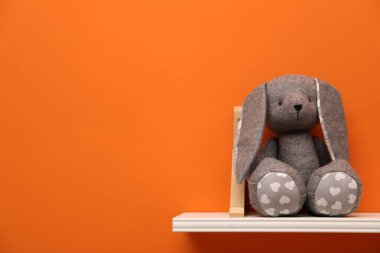 Turuncu duvarda oyuncak tavşanı olan beyaz raf, metin için boşluk