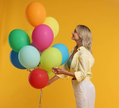 Sarı arka planda renkli balonları olan mutlu bir kadın.