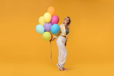 Sarı arka planda renkli balonları olan mutlu bir kadın.