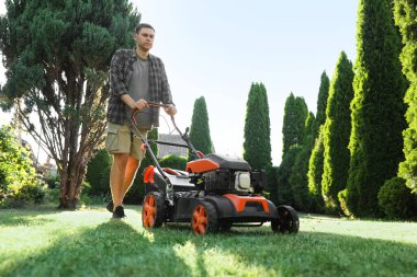 Bahçede çim biçme makinesiyle yeşil çim biçen adam, düşük açılı görüş.