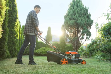 Bahçede çim biçme makinesiyle yeşil çim biçen bir adam