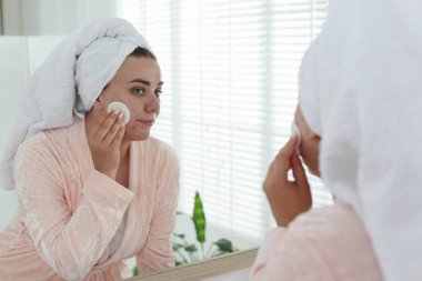 Sivilceli bir kadın aynanın içinde yüzünü temizliyor.