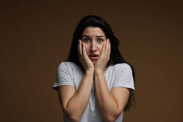 Worried woman suffering from panic attack on brown background
