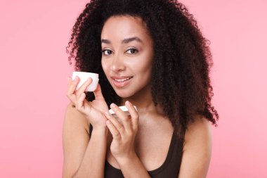 Güzel Brezilyalı kadın pembe arka planda bir kavanoz kolajen kremi ile