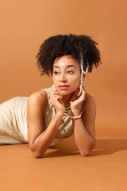 Açık kahverengi arka planda şık giyinmiş güzel Brezilyalı bir kadının moda portresi.