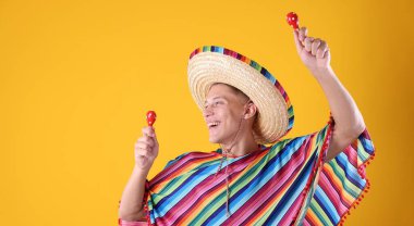 Şapkalı mutlu bir adam ve sarı arka planda marakas çalan renkli bir panço. Metin için boşluk