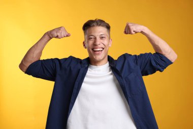 Kuvvet. Sarı arka planda kaslarını gösteren mutlu bir adam.