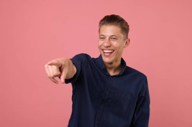 Yakışıklı adam gülüyor ve pembe arka plandaki bir şeye işaret ediyor. Pozitif duygu
