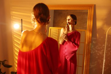 Güzel bir kadın içeride aynanın yanında ruj sürüyor.