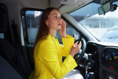 Hazırlanıyor. Arabada aynaya bakan genç bir kadın.