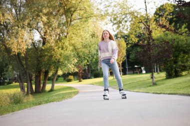 Güzel genç bir kadın parkta paten kayıyor.