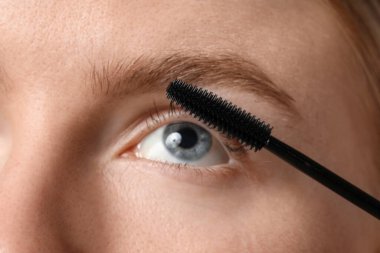 Genç bir kadın kirpiklerine rimel sürüyor, yakın plan.