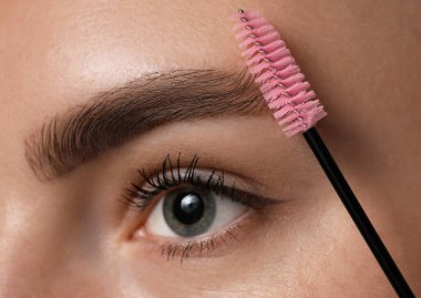 Genç bir kadın kaşlarını hortlakla fırçalıyor, yakın plan.