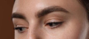 Kahverengi arka planda güzel kaşları olan genç bir kadın, yakın plan.