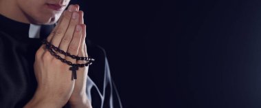 Karanlık arka planda tespih çeken bir rahip, yakın plan. Metin için boşluk