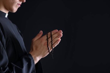 Siyah arka planda tespih çeken bir rahip, yakın plan. Metin için boşluk